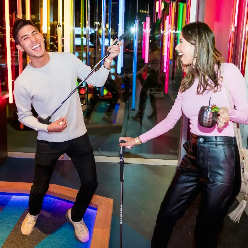 A happy man holding his putt like a guitar and a woman holding a drink and putt