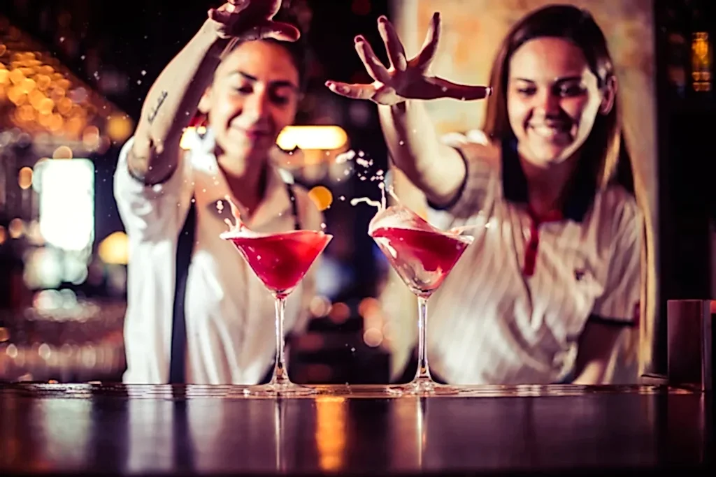 Two women are messing around with two red cocktails