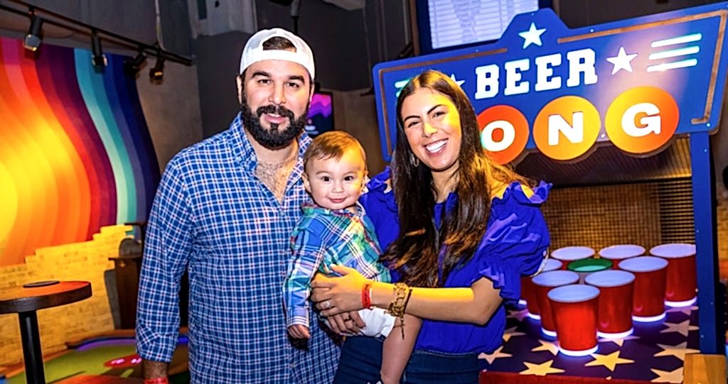 Dad and Mom holding their baby in front of the Beer Pong hole